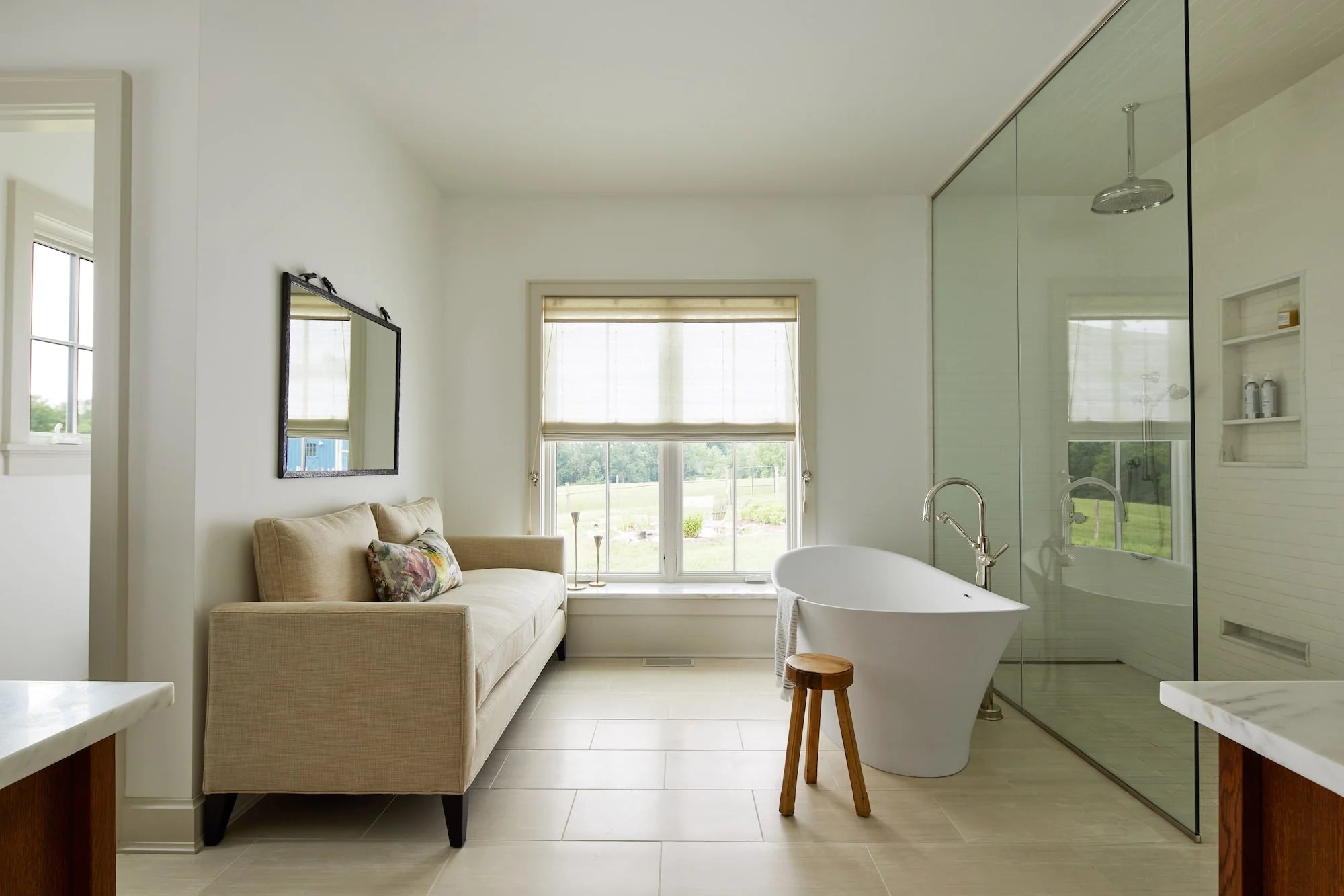 Spacious bathroom at Cold Brook Farm with freestanding tub, walk-in glass shower, linen sofa, and natural light from large windows.