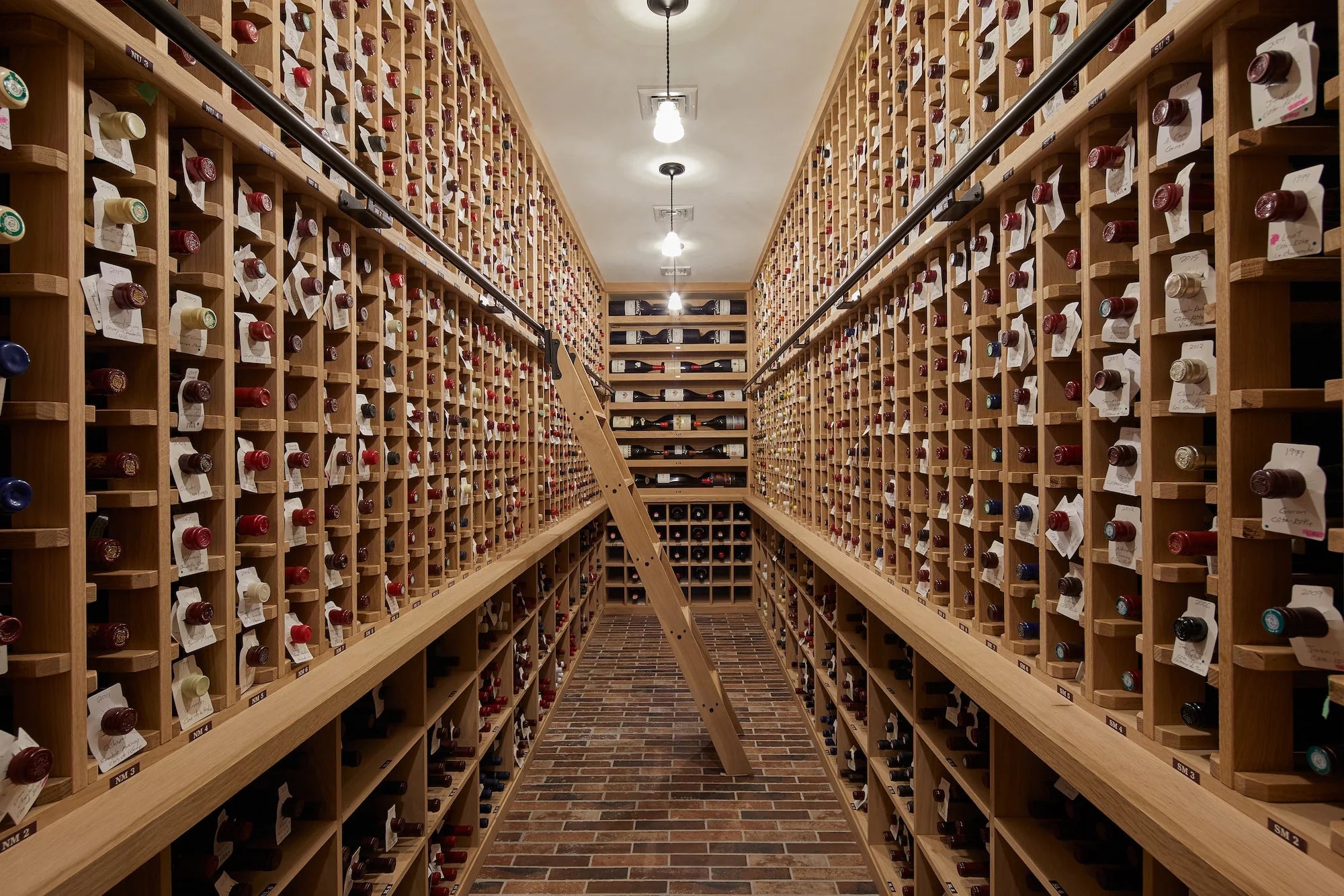 Expansive wine cellar at Cold Brook Farm with brick flooring, custom wood racks, rolling ladder, and hundreds of curated wine bottles.