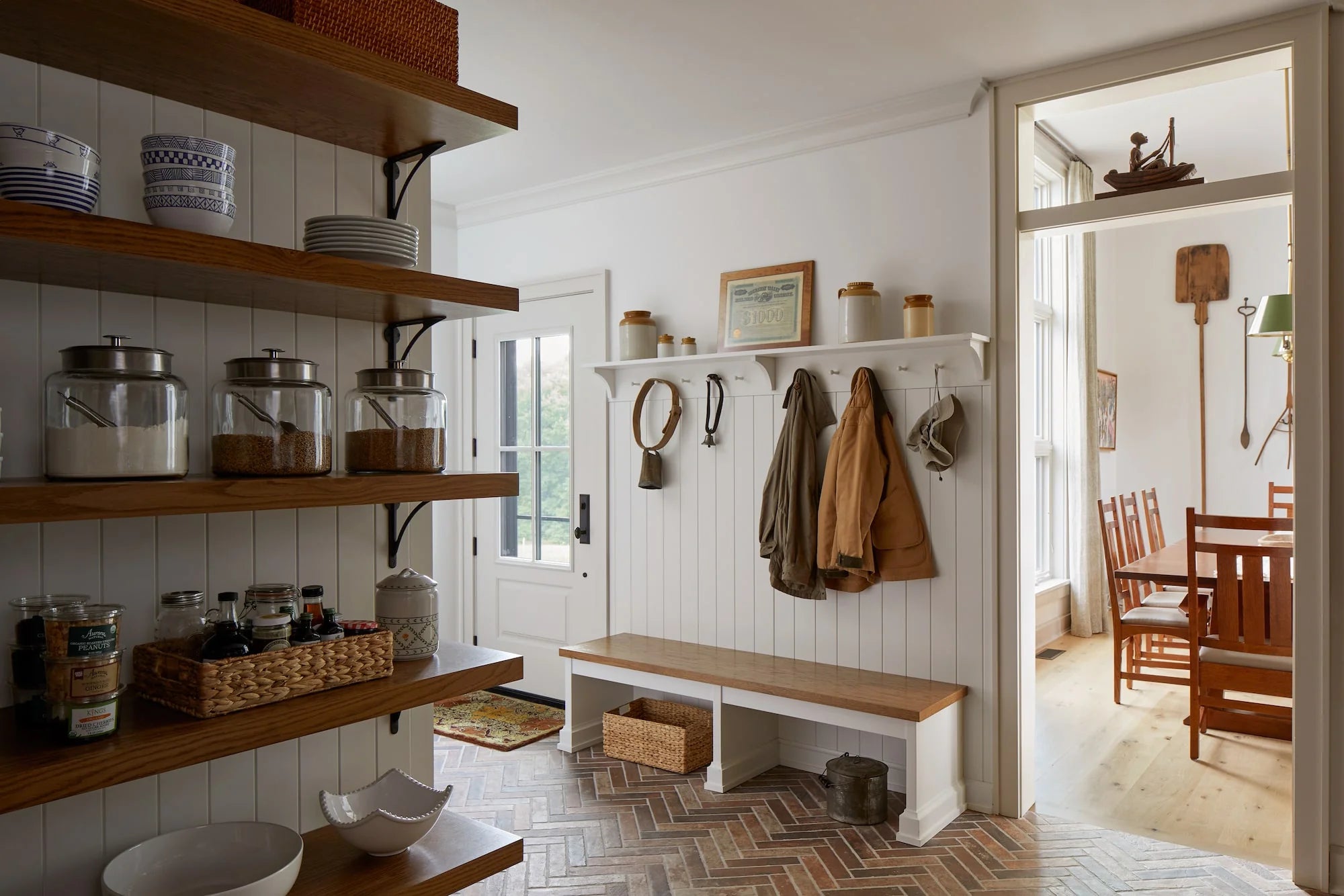 Farmhouse mudroom at Cold Brook Farm with herringbone brick floors, open pantry shelving, coat hooks, and bench seating.