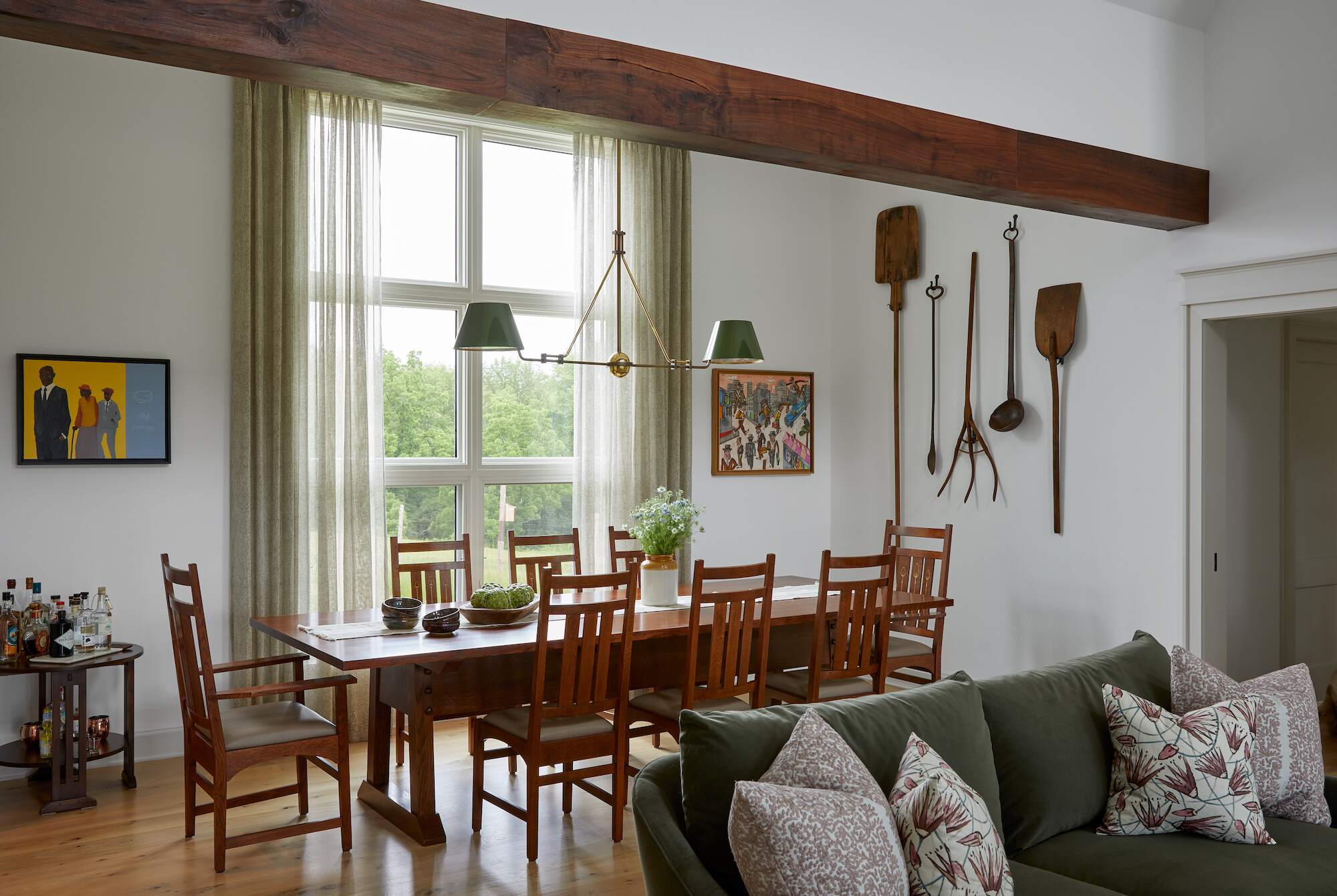 Farmhouse dining room at Cold Brook Farm with long wood table, ladder-back chairs, vintage kitchen tools on the wall, and large picture window.