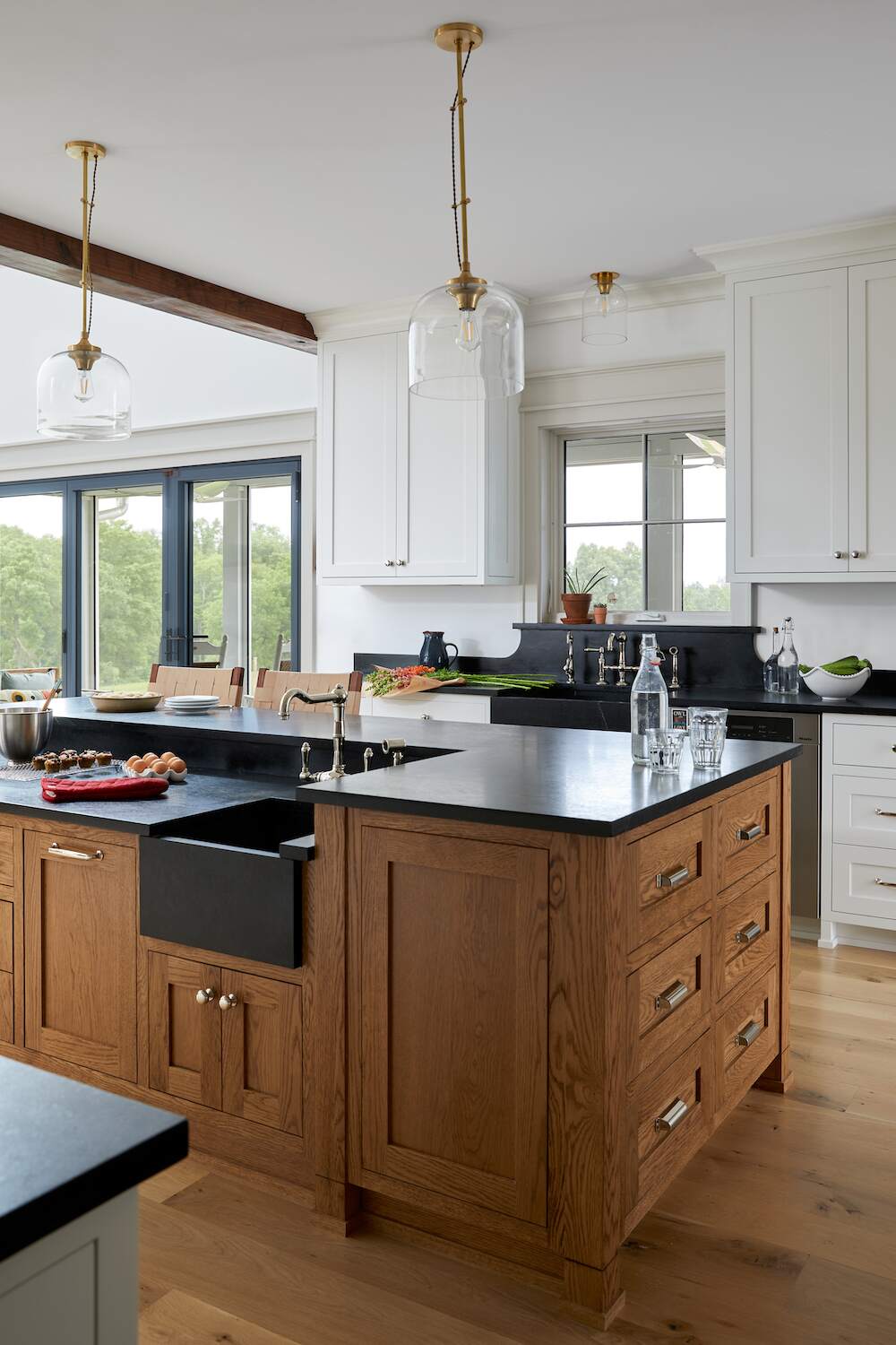 Close-up of Cold Brook Farm kitchen island with black soapstone counters, oak cabinetry, farmhouse sink, and glass pendant lights.