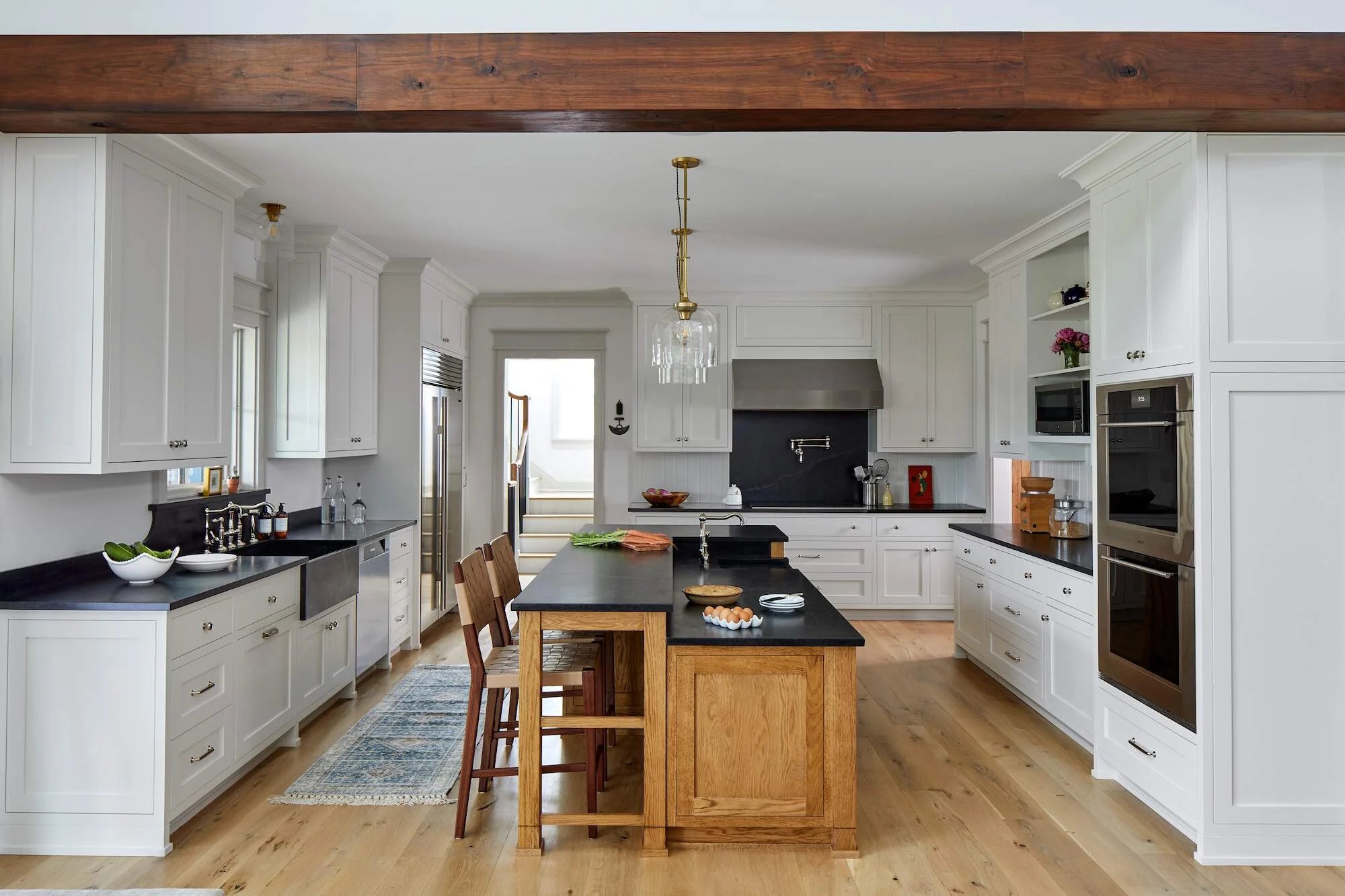 Farmhouse kitchen at Cold Brook Farm featuring white cabinetry, black countertops, oak island, farmhouse sink, and brass pendant lighting.