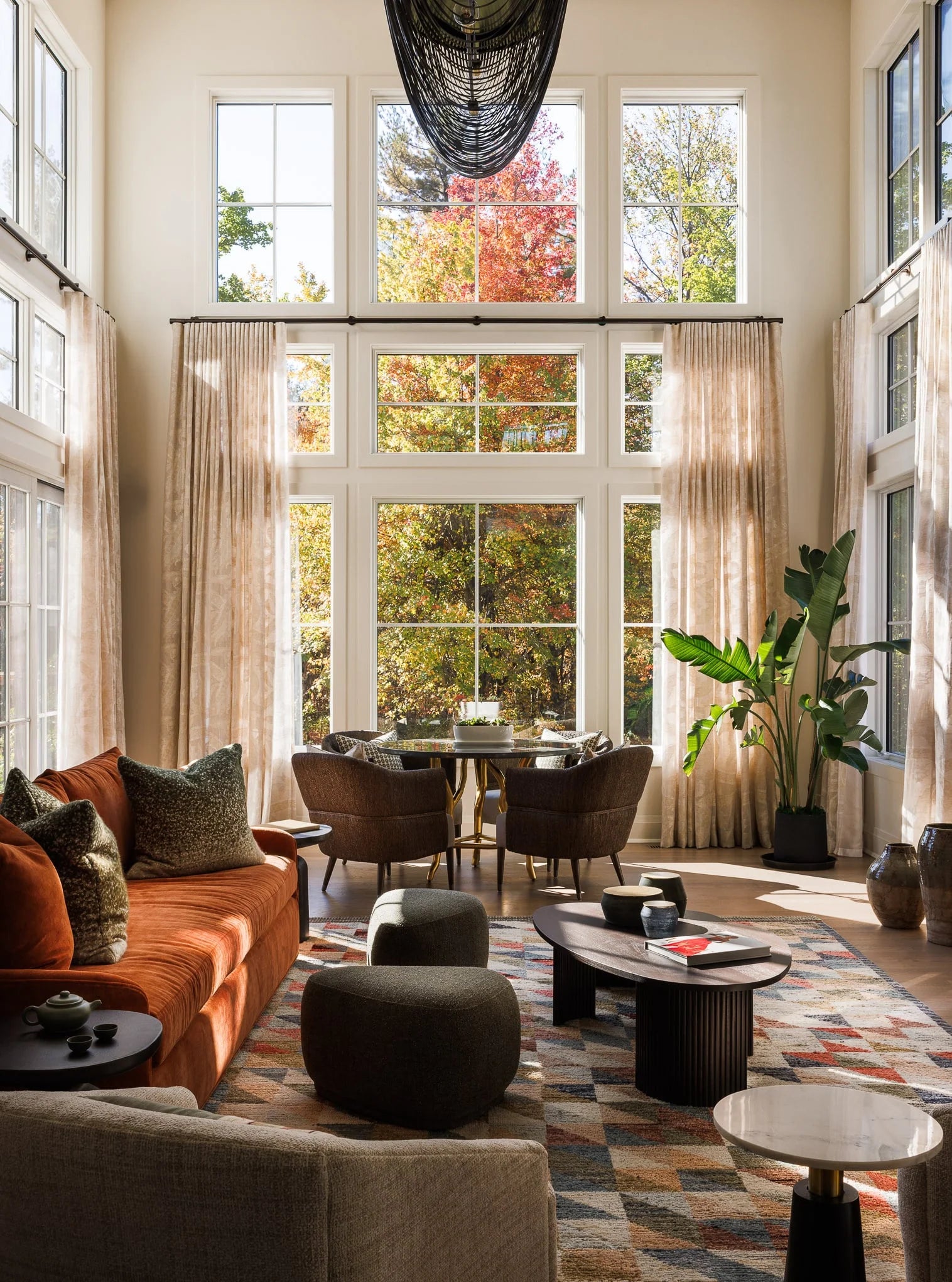 Twin Brooks living room with rust-colored sofa, geometric rug, and floor-to-ceiling windows framing vibrant autumn views.