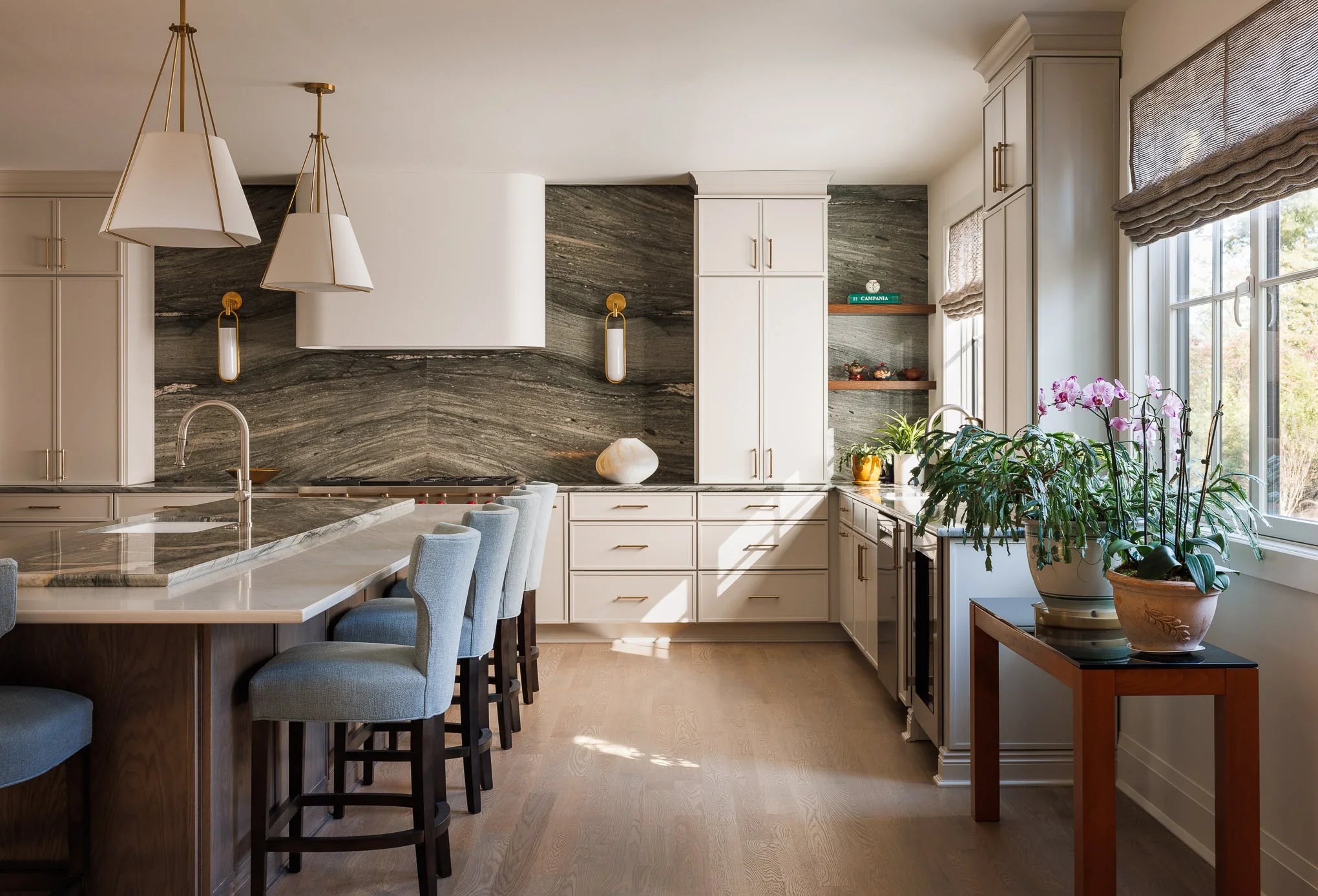 Bright kitchen featuring a striking stone backsplash, white cabinetry, large island with marble countertop, and blue upholstered barstools.