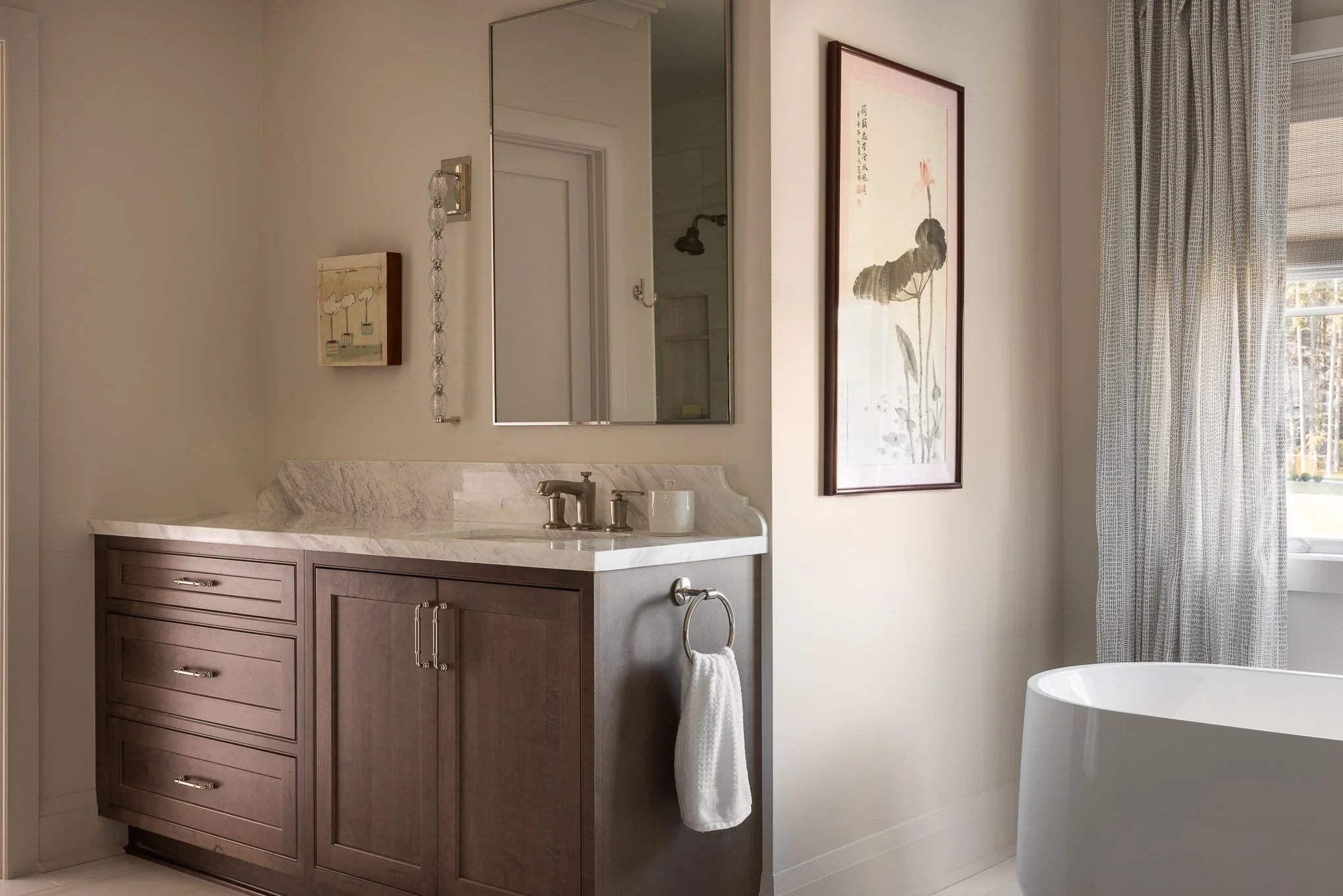 Bathroom with dark wood vanity, marble countertop, large mirror, and framed botanical artwork beside a modern freestanding tub.