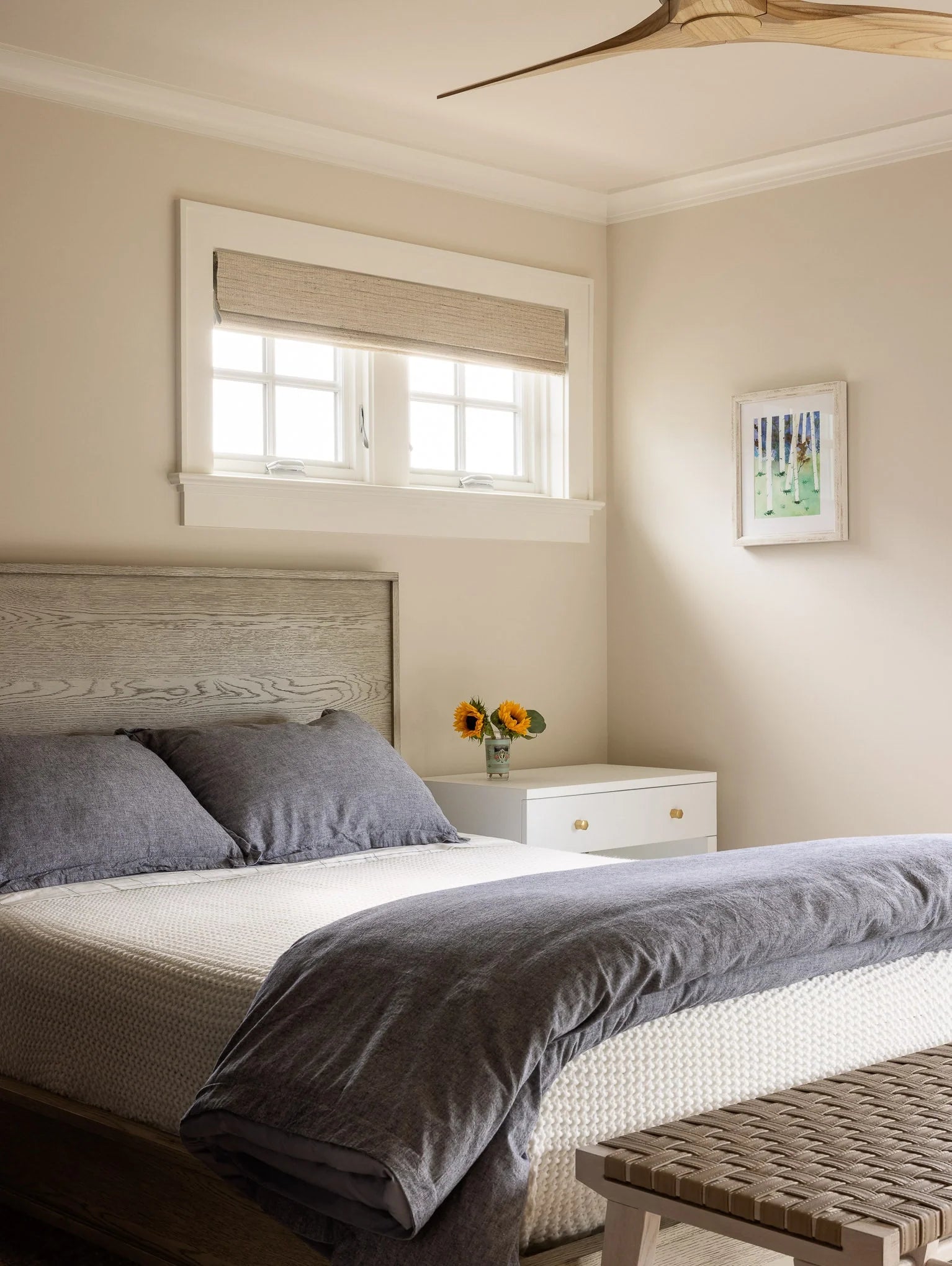 Minimalist bedroom with gray wood bed, soft gray linens, and sunflowers on white nightstand.