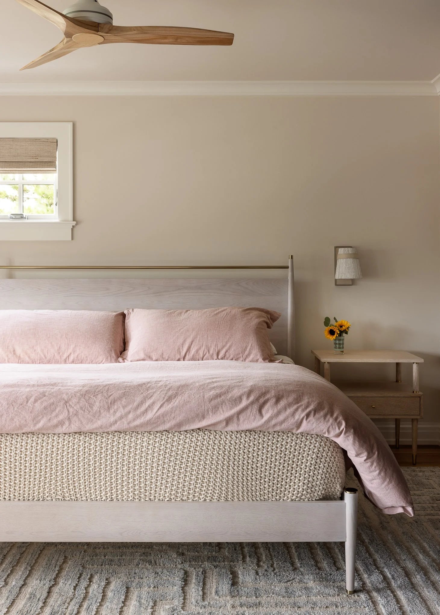 Neutral bedroom featuring light wood bed frame, blush pink bedding, and woven rug.