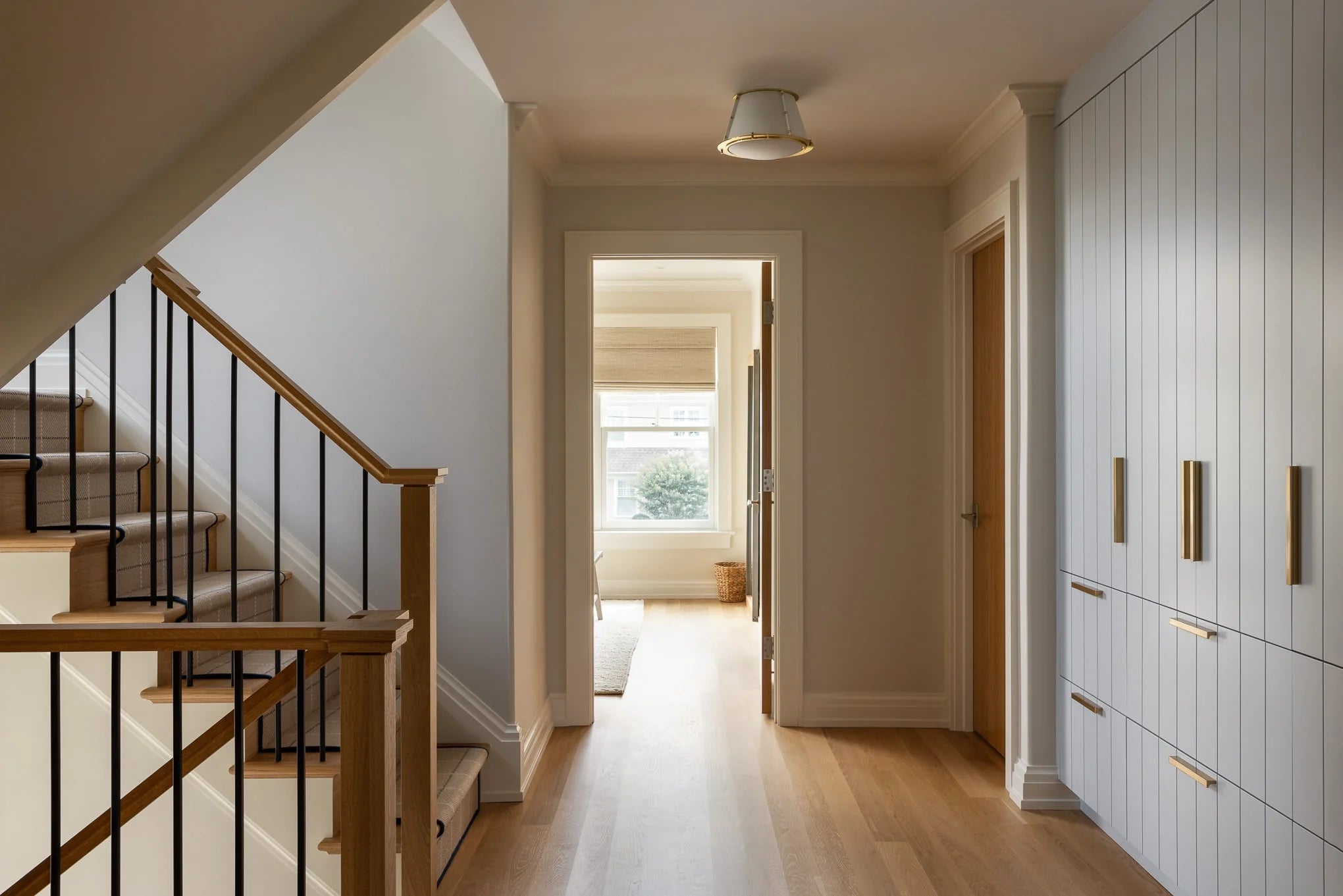Modern hallway with white paneled storage cabinets, gold hardware, and wood staircase.