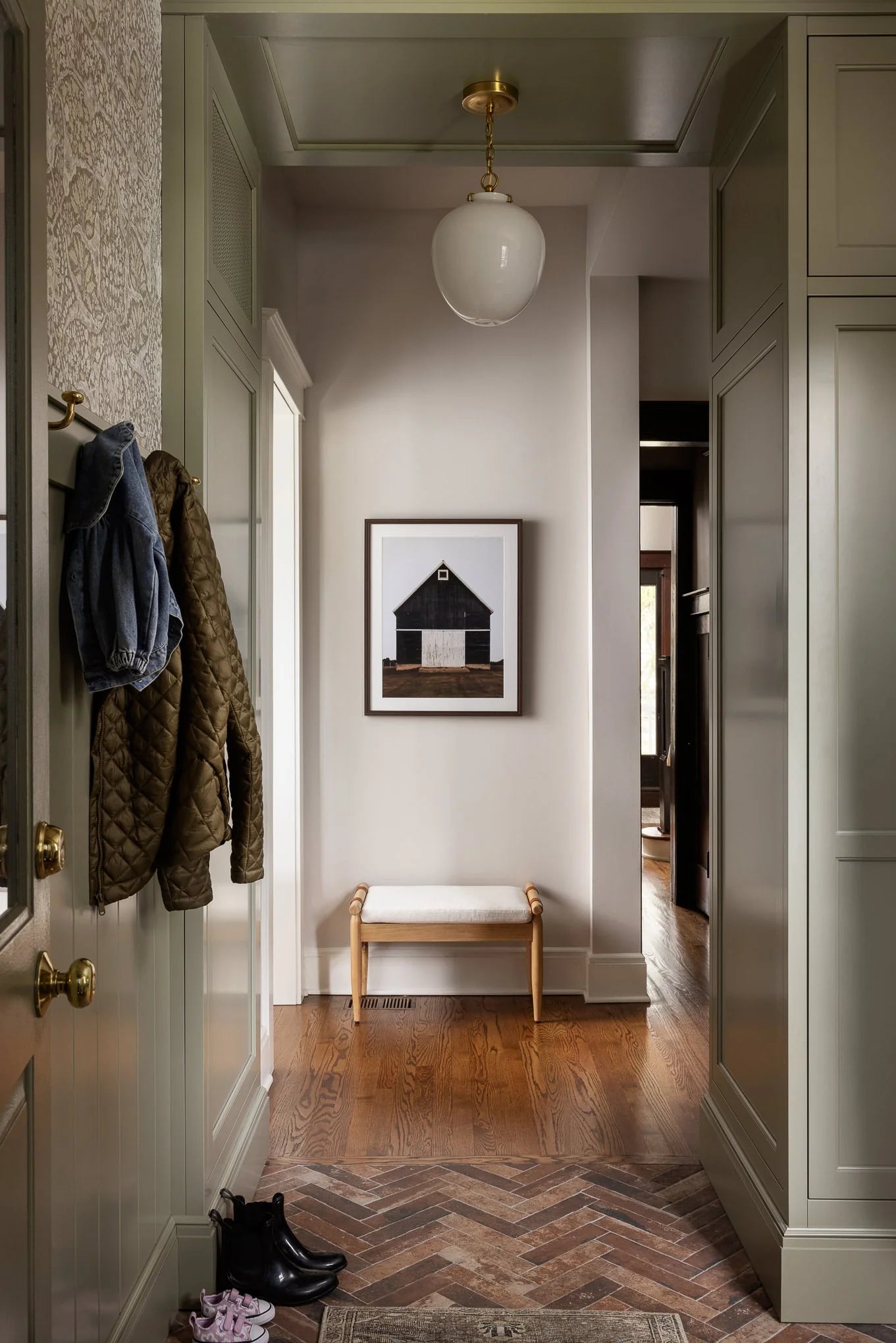 Lawrence mudroom with herringbone tile floor, built-in cabinetry, wall hooks, and a framed barn photograph above a simple wood bench.