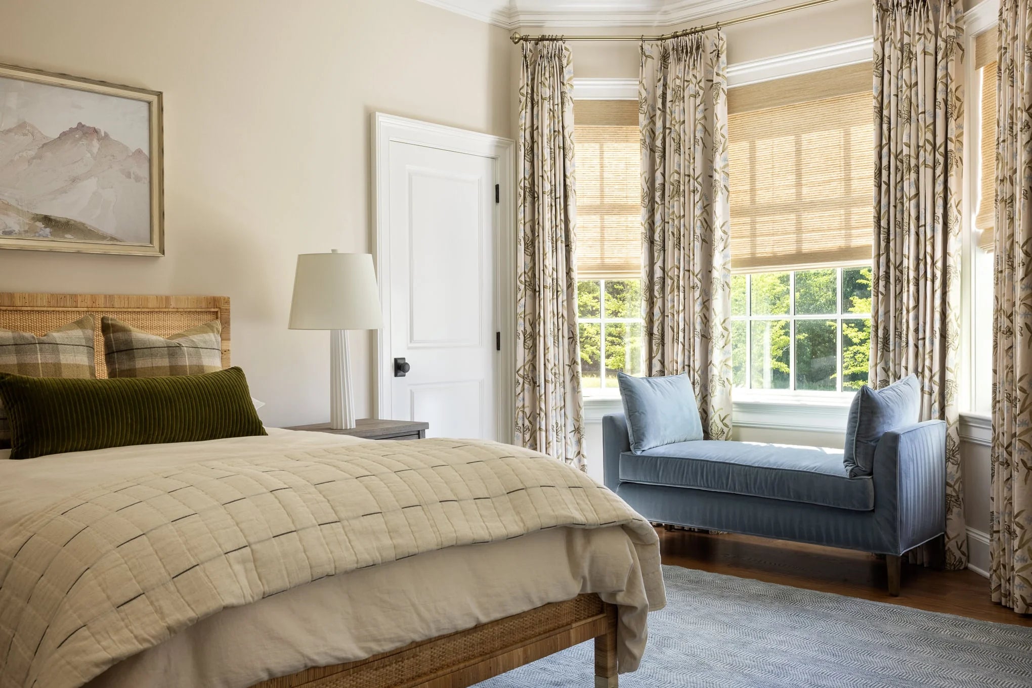 Serene bedroom with woven headboard, neutral bedding, and blue upholstered bench by windows at Moonlight project.