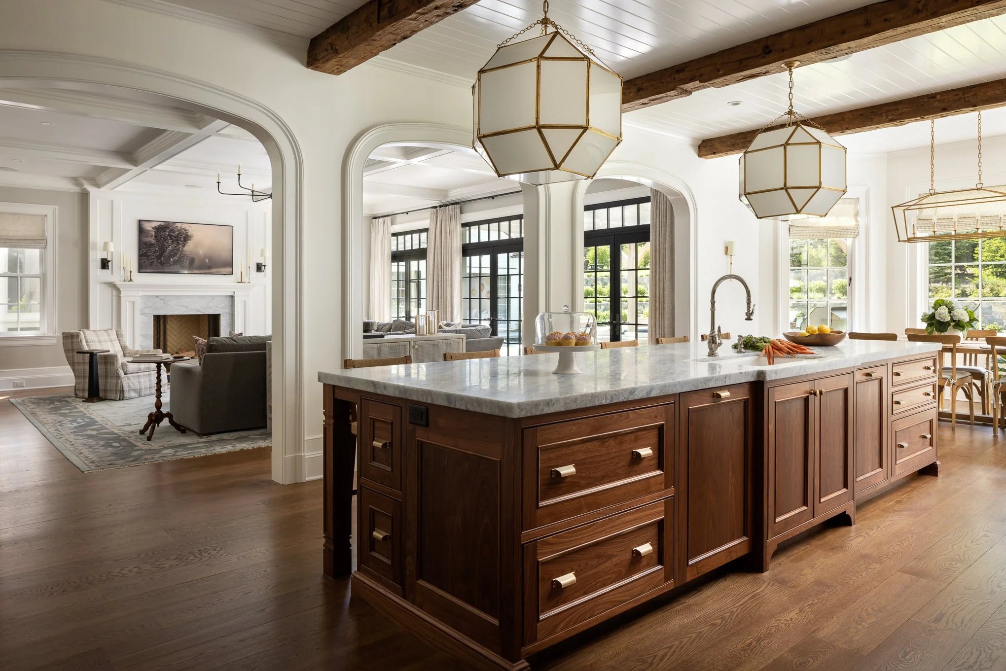 Open-concept kitchen with marble island and view into living room with coffered ceiling and fireplace at Moonlight project.