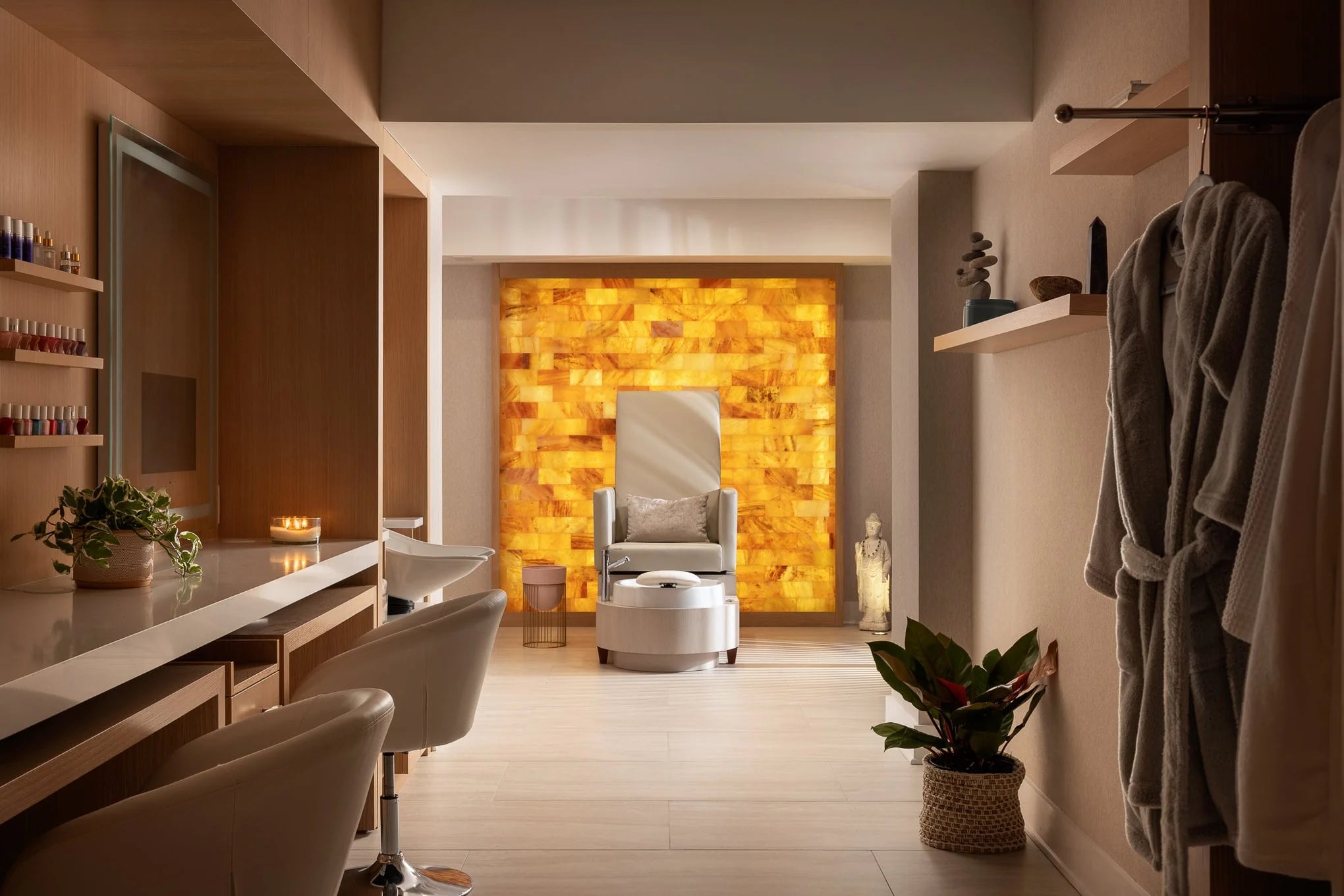 Modern spa-inspired space at Essex House featuring a pedicure chair framed by a glowing amber backlit wall, wood cabinetry, and soft neutral tones.