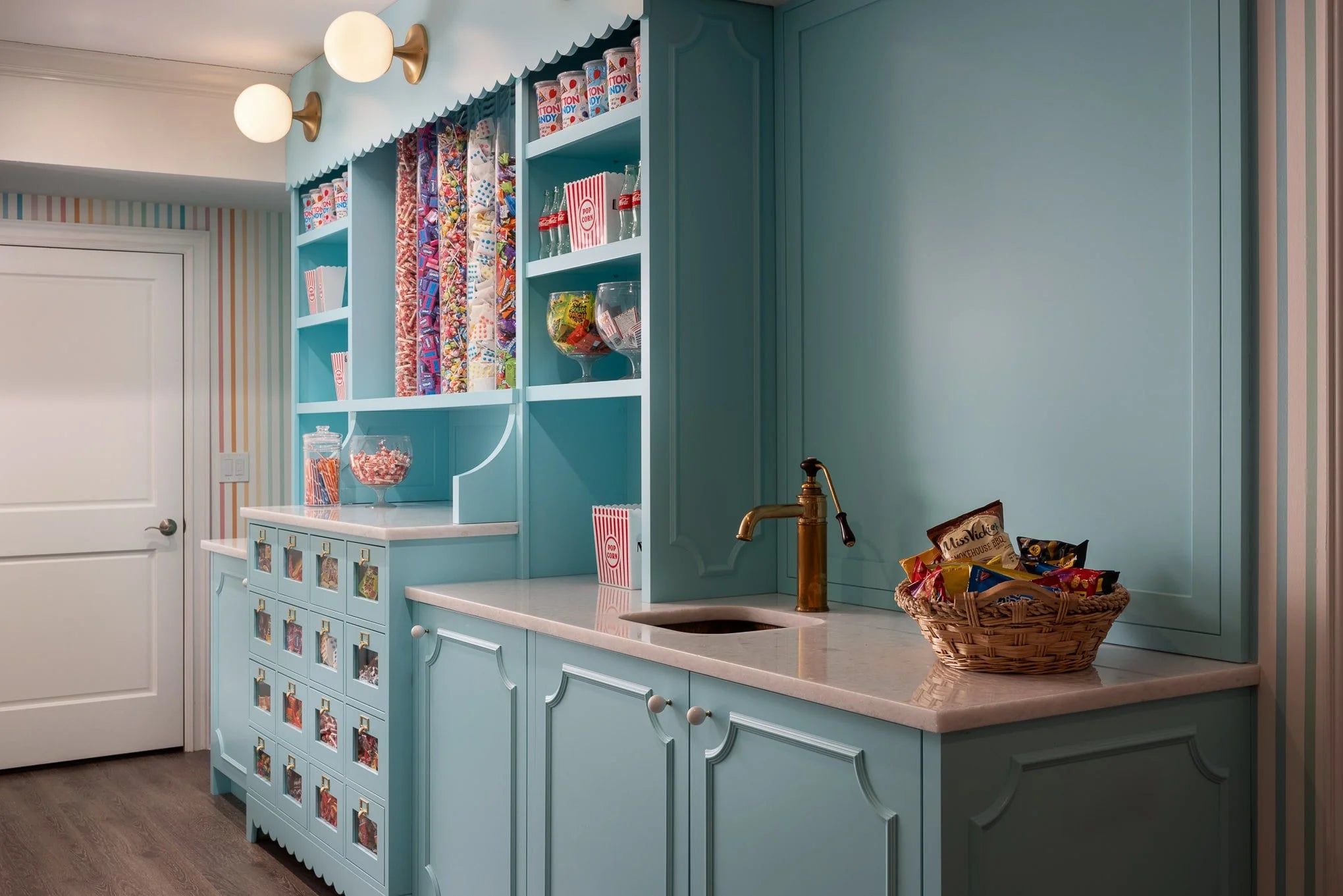 Playful candy bar at Essex House with pastel blue cabinetry, glass jars filled with colorful sweets, brass fixtures, and striped wallpaper accents.
