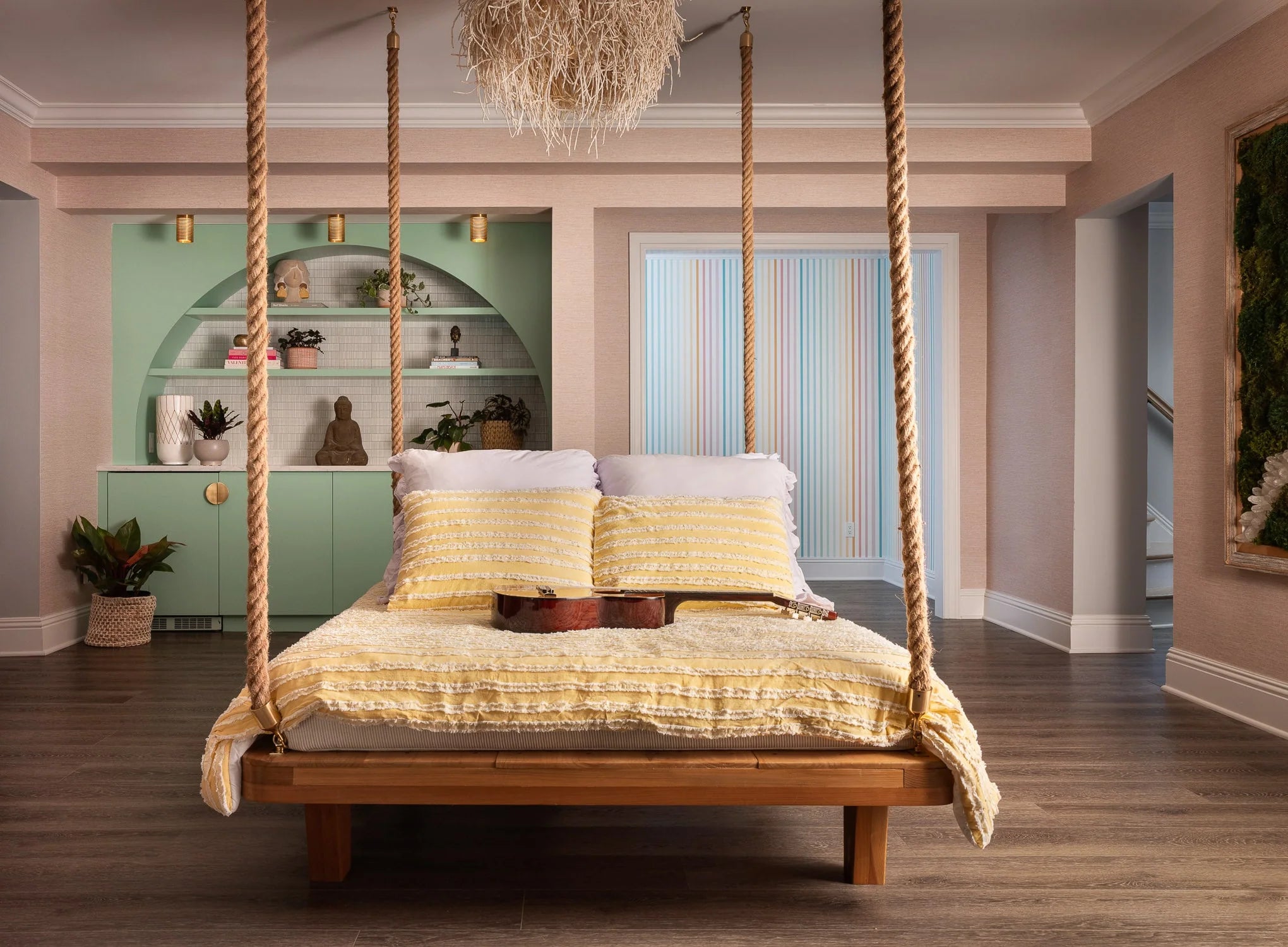Cozy bedroom at Essex House with a rope-hung wooden swing bed, soft yellow bedding, and built-in mint green shelving styled with plants and sculptures.