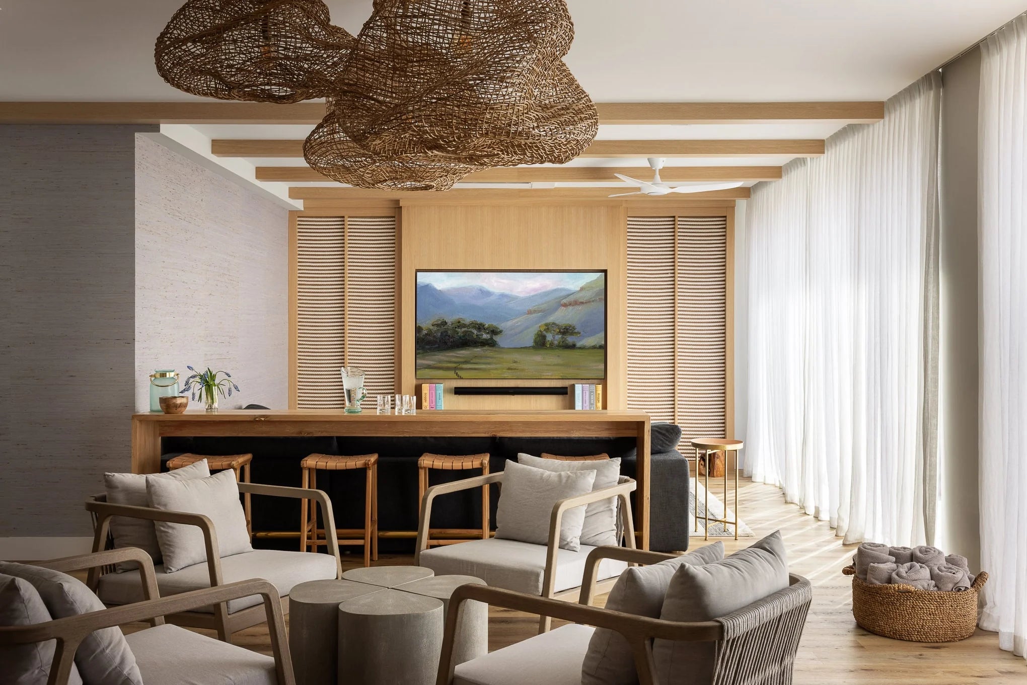 Cozy living space at Essex House with woven statement light fixtures, neutral armchairs, a built-in wood entertainment wall, and floor-to-ceiling sheer curtains framing natural light.