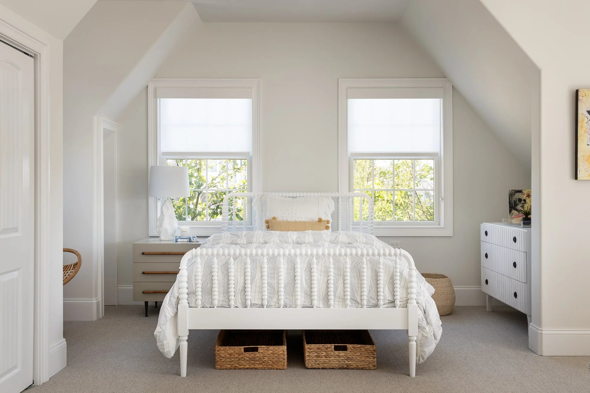 Bright guest bedroom with white spindle bed, wicker storage baskets, and double windows.