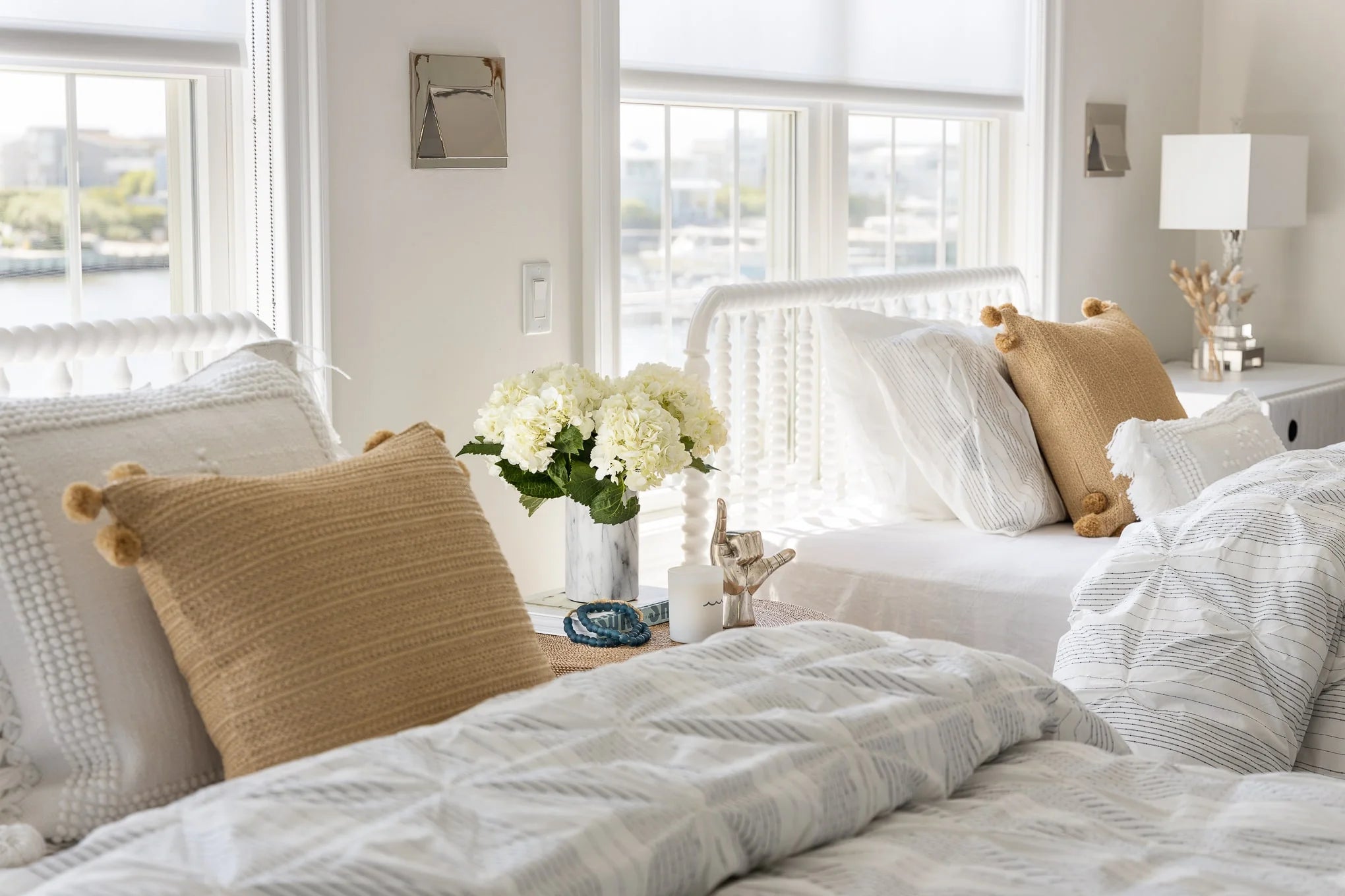 Close-up of twin beds styled with white textured bedding, tan accent pillows, and a marble vase of white hydrangeas on the bedside table.