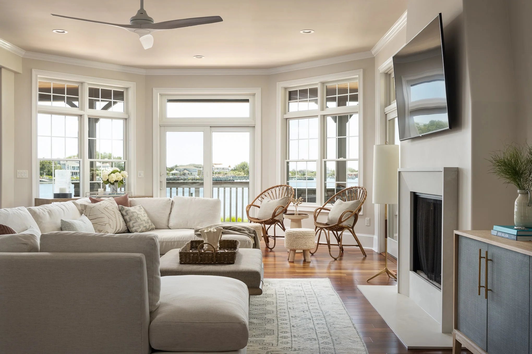 Living room with sectional sofa, rattan chairs, fireplace, and large windows overlooking water views.