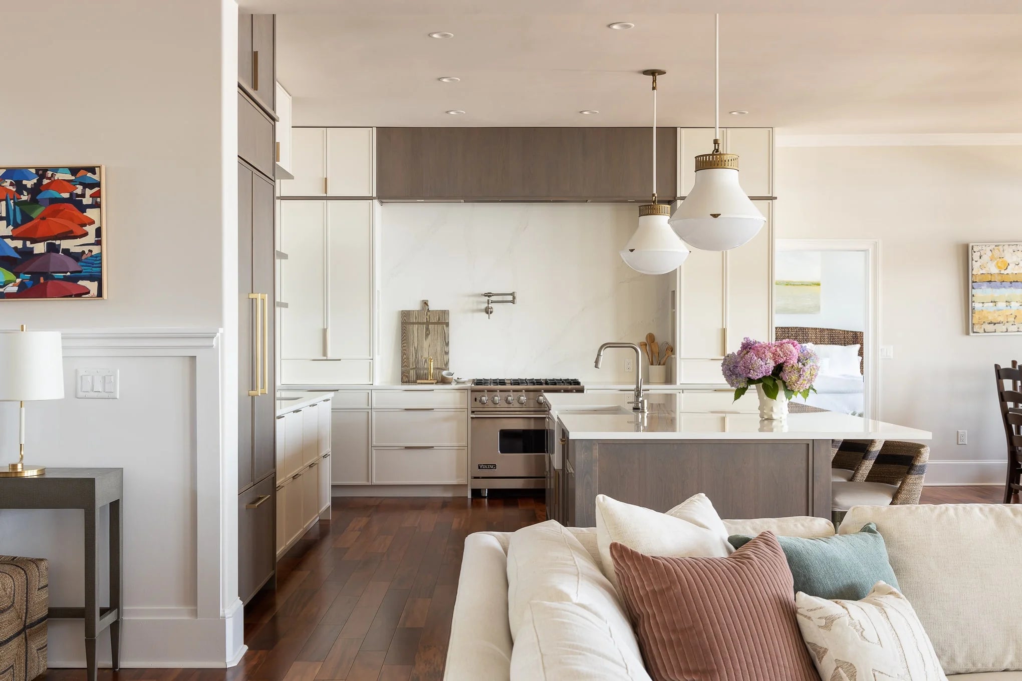 View into kitchen from living room with neutral sofa, pendant lights, and wood cabinetry.
