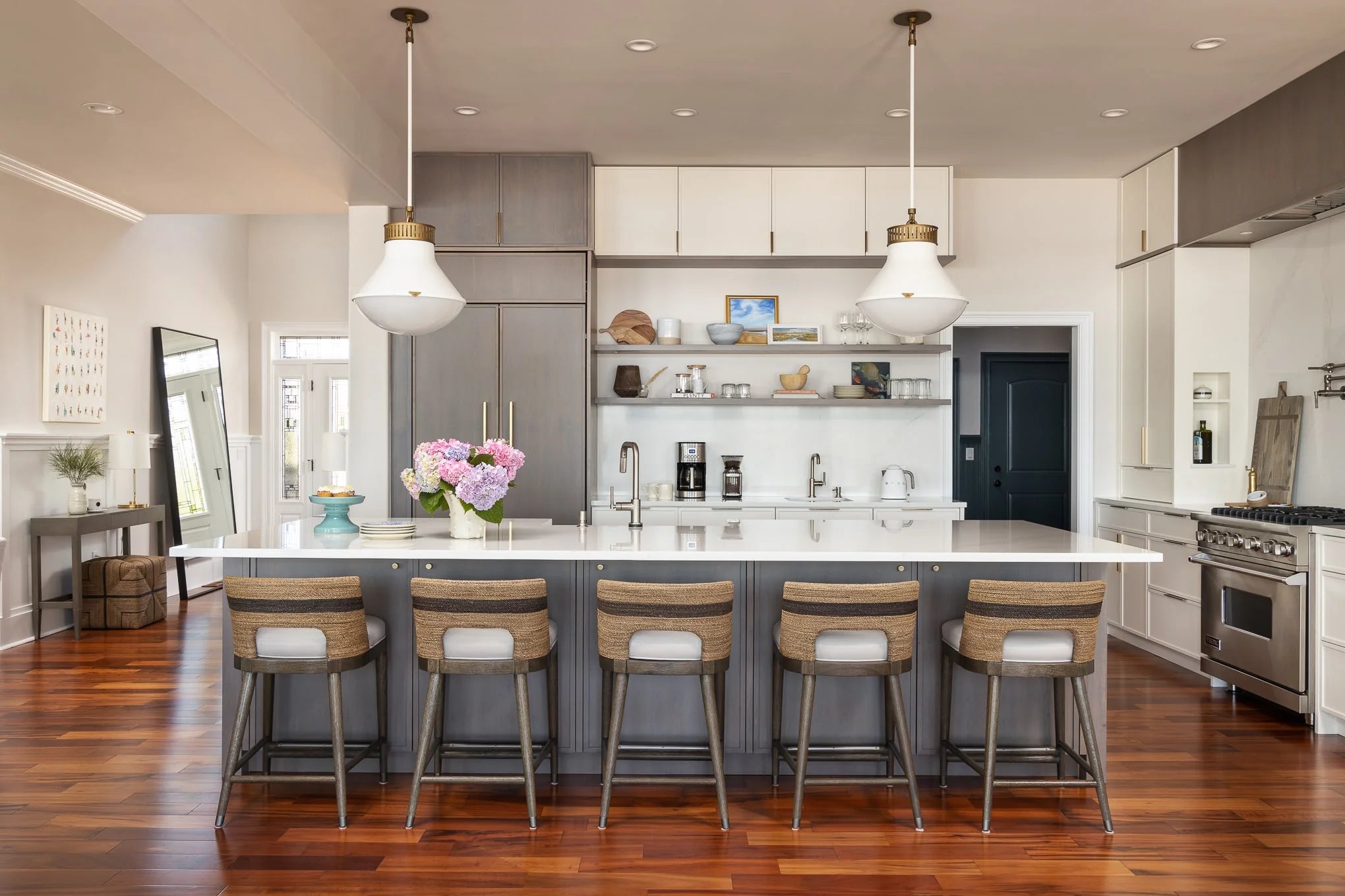 Open kitchen design with gray and white cabinetry, floating shelves, large island, and warm hardwood floors – Haven Bay coastal renovation.
