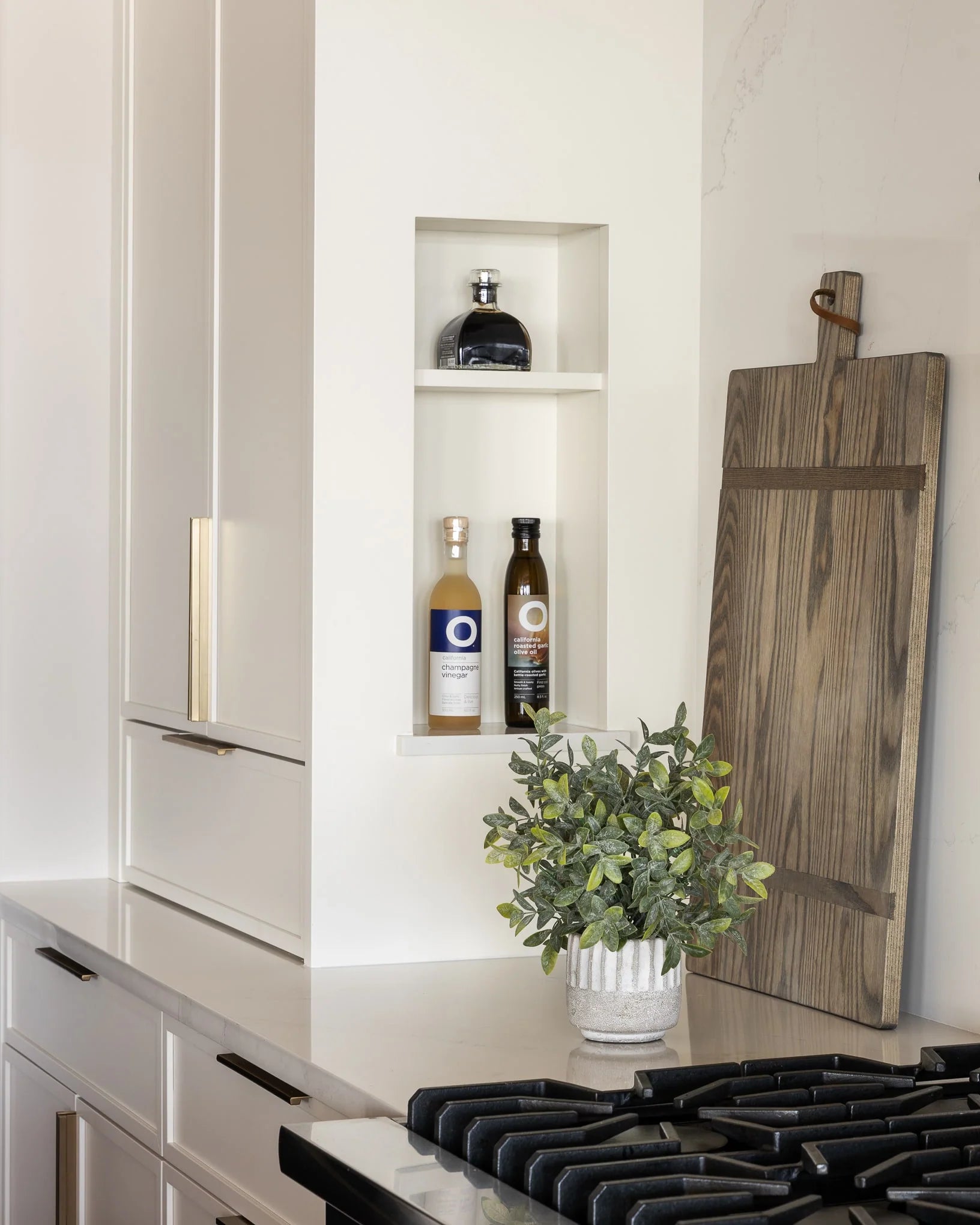 Custom kitchen niche with champagne vinegar and olive oil bottles, wood cutting board, and potted plant on quartz countertop – Haven Bay project.
