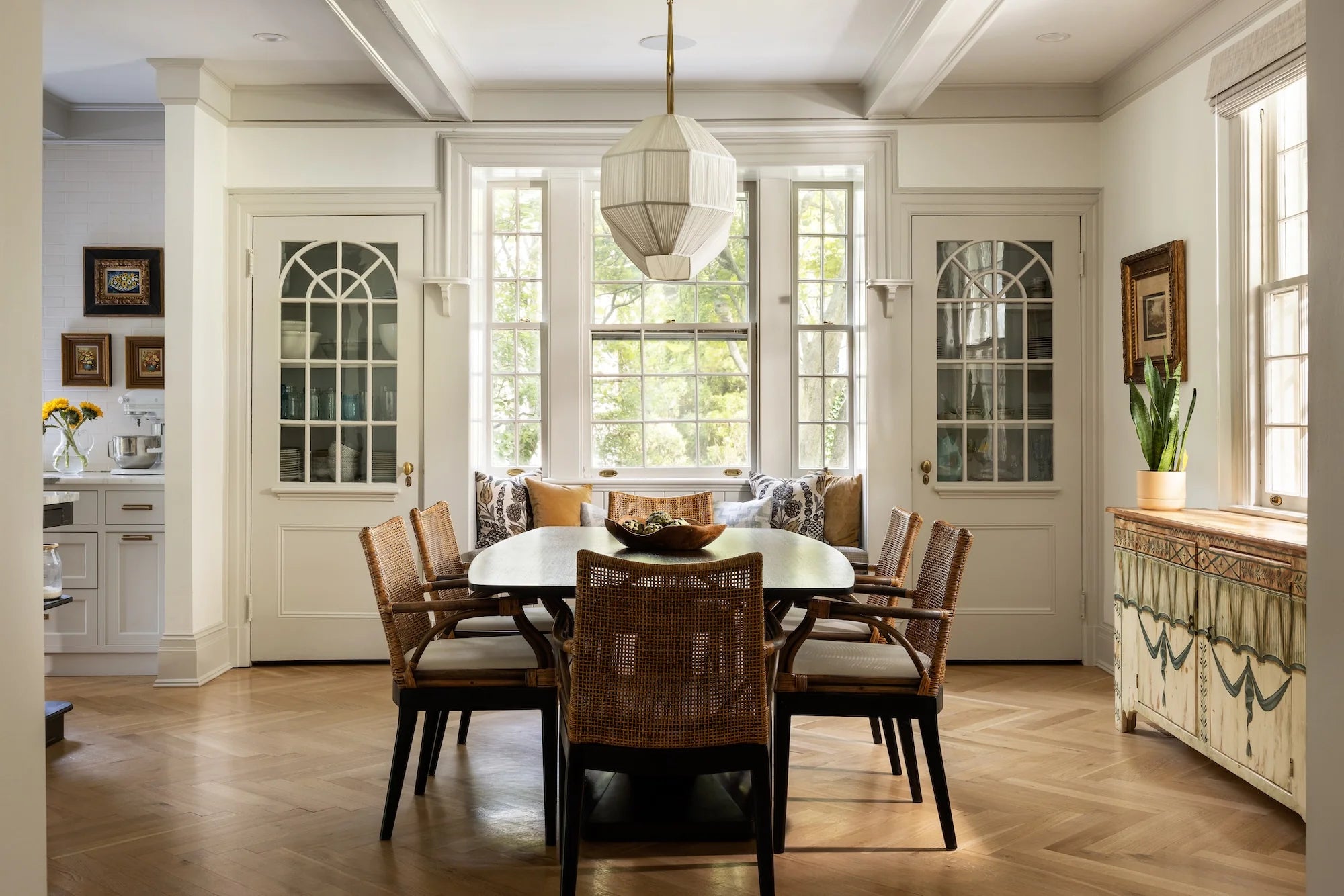 Stoneleigh dining room by AHD&Co featuring woven chairs, arched glass cabinets, bay window seating, and a sculptural pendant light.