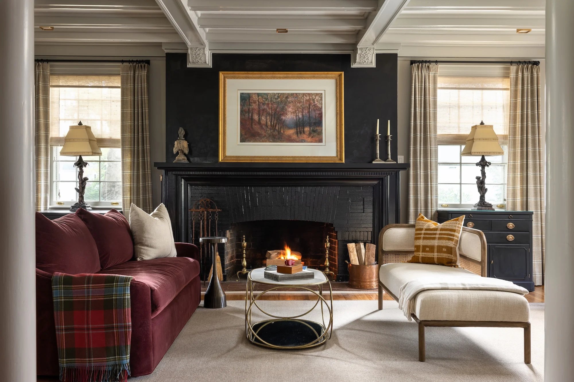 Stoneleigh living room by AHD&Co featuring black fireplace with artwork, burgundy sofa, upholstered daybed, and layered traditional details.