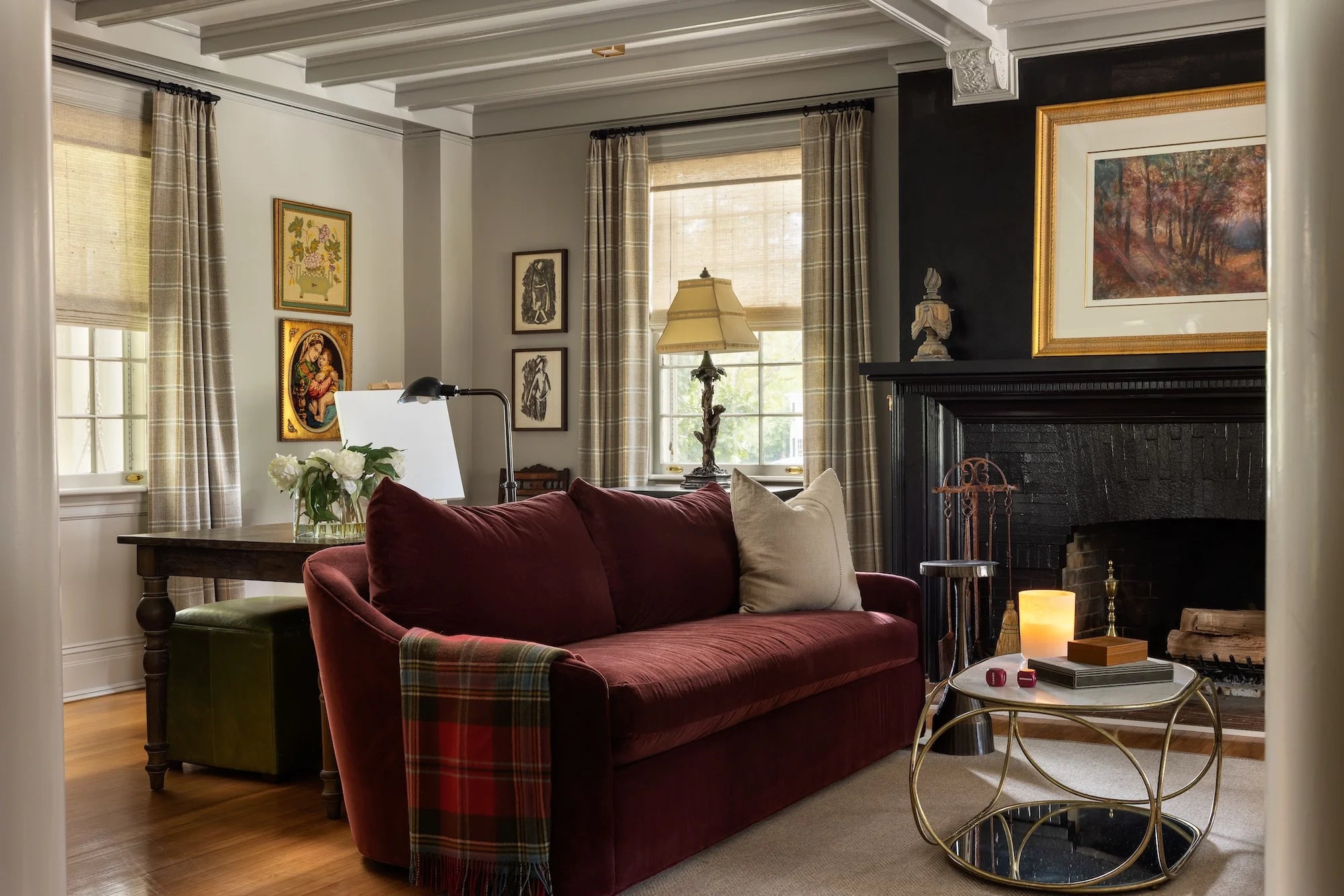 Stoneleigh Westfield NJ living room renovation by AHD&Co with burgundy sofa, plaid throw, writing desk, and black painted fireplace surround.