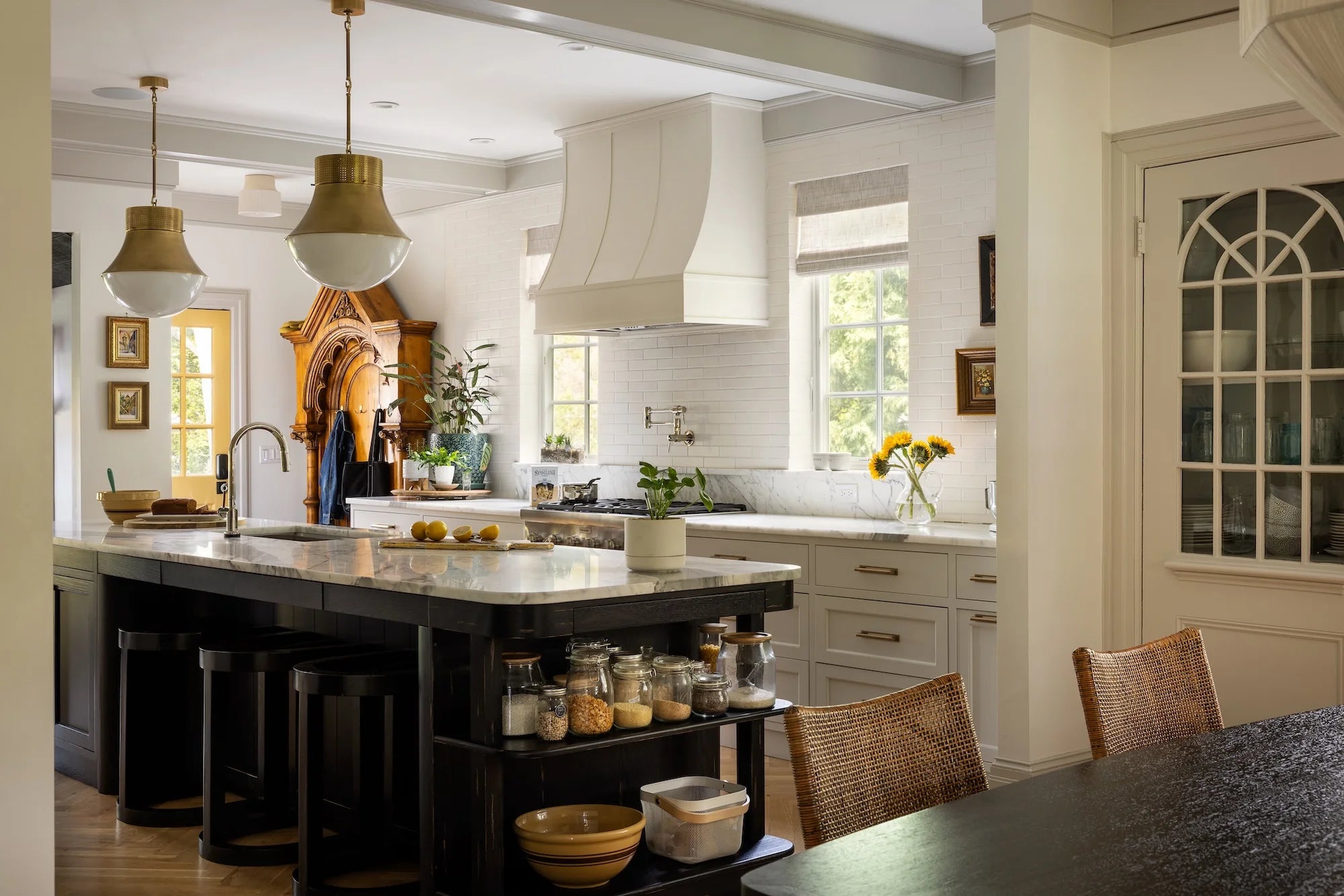 Stoneleigh kitchen design by AHD&Co with white cabinetry, marble counters, sunflowers, and a dark island with open shelving and brass lighting.