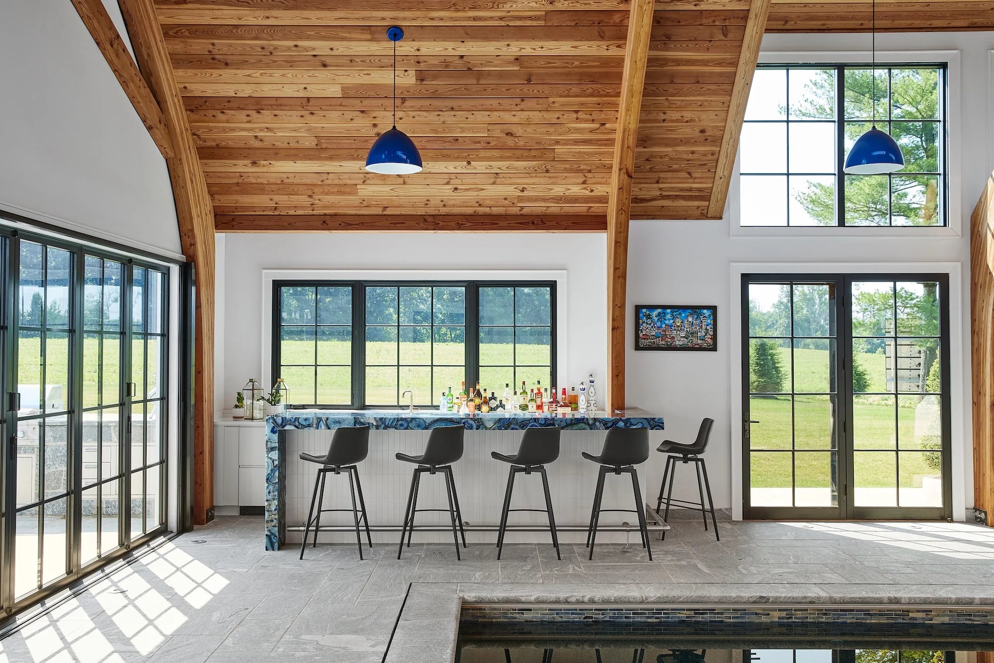 Indoor pool house with wood ceiling, marble-topped bar, and black stools at Airport Road residence