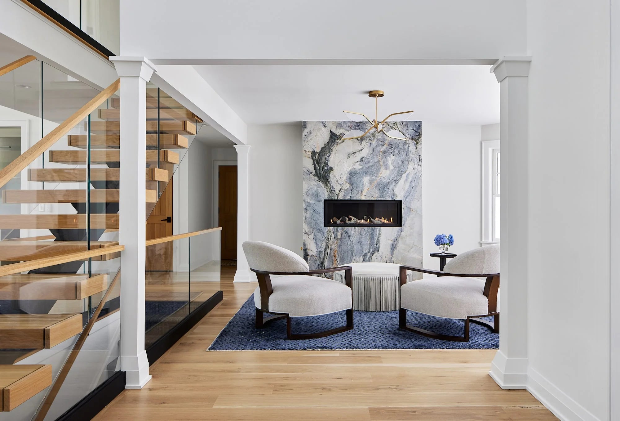 Modern floating wood staircase with glass railing and marble fireplace feature in Airport Road home