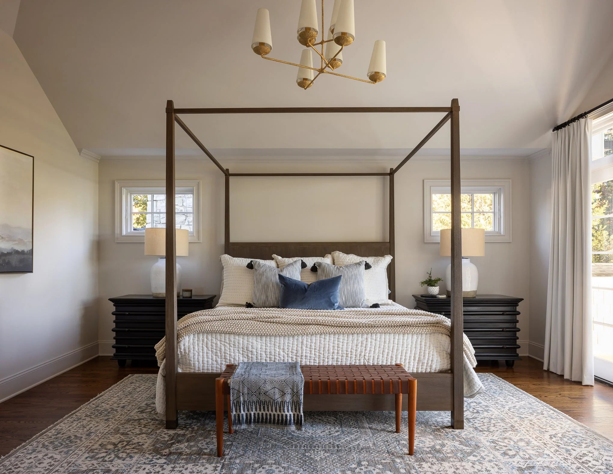 Primary bedroom with four-poster bed, layered neutral bedding, accent pillows, and a large area rug.