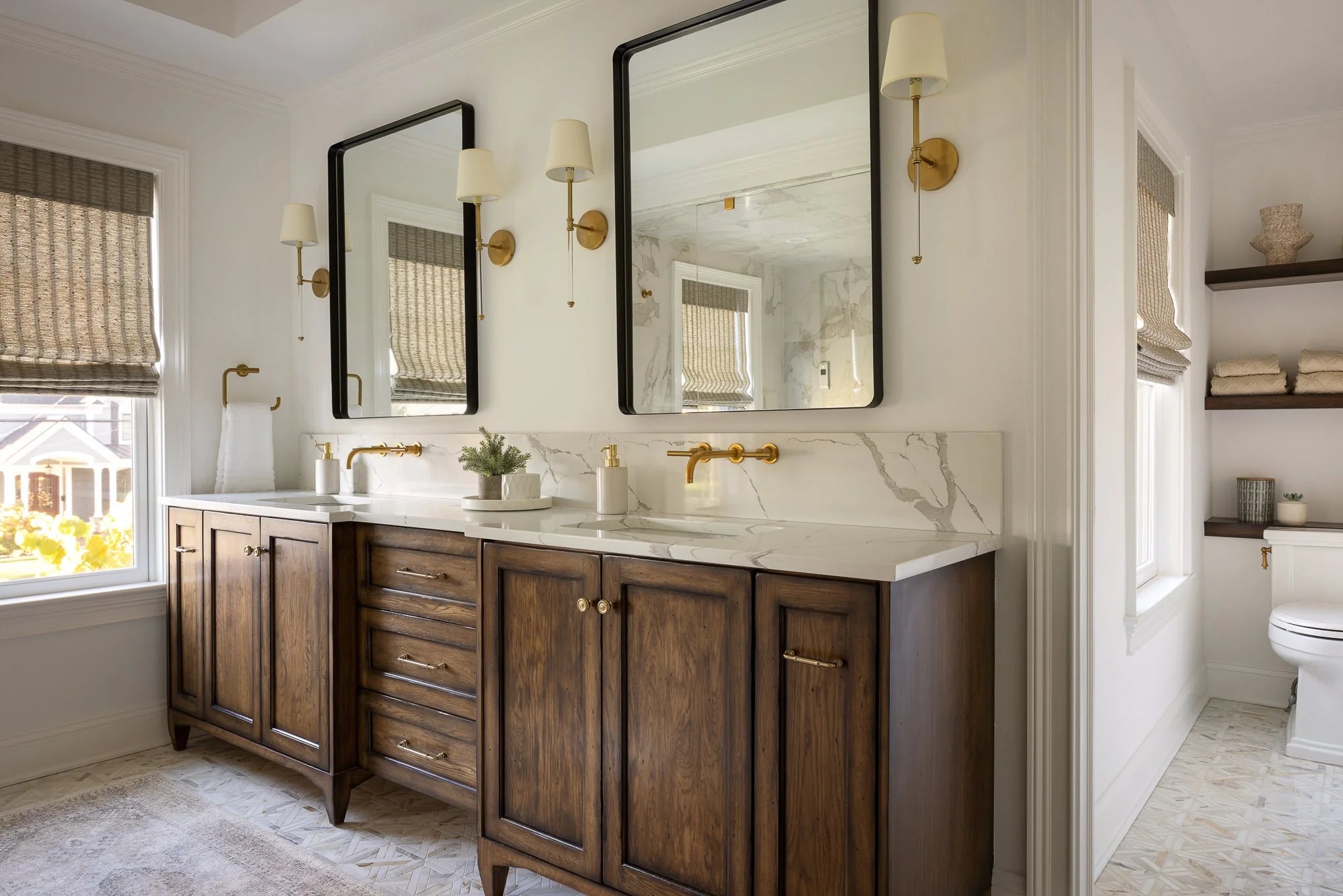 Double vanity bathroom with wood cabinets, marble countertops, brass fixtures, and dual framed mirrors.