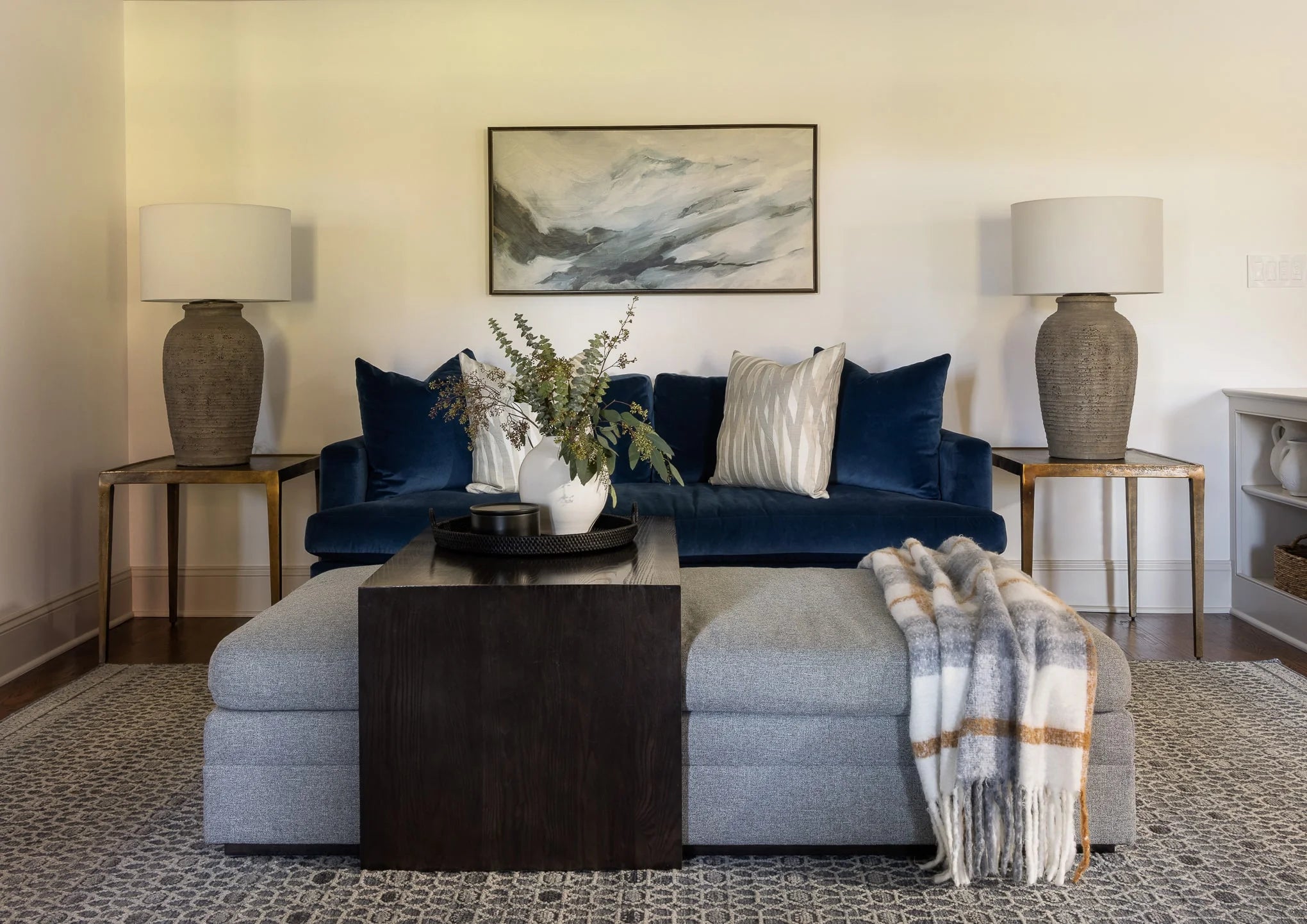 Cozy seating area with a blue velvet sofa, neutral pillows, twin stone lamps, and a dark wood coffee table with greenery centerpiece.
